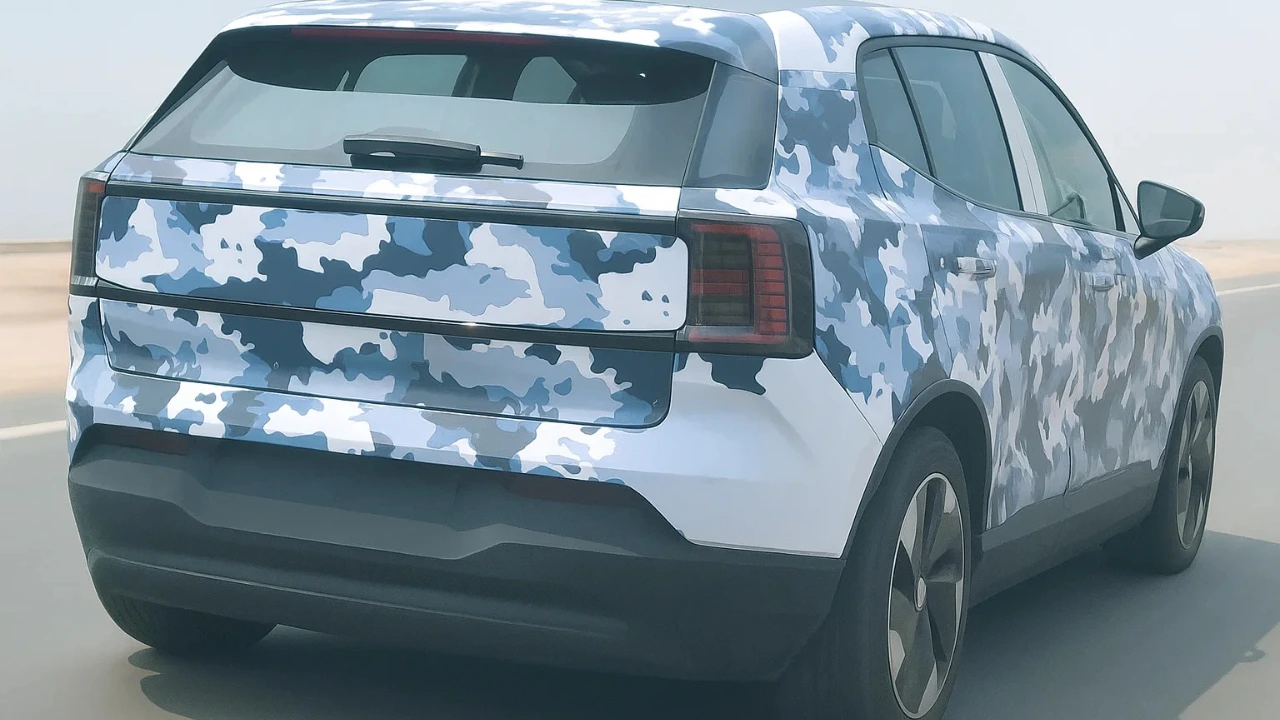 Volvo EX30 Electric SUV spy shot on road, camouflaged in blue and white, showing rear design and taillights during testing.